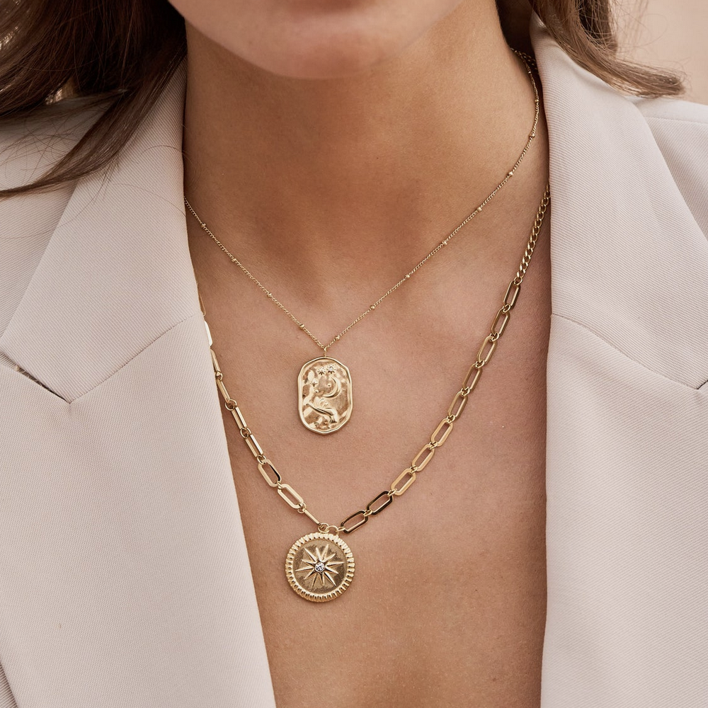 Collier doré composé d'un pendentif en forme géométrique avec différents motifs : main, soleil, lune et étoile, et d'un strass blanc 40+5 cm