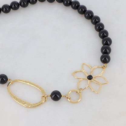 Collier doré composé d'un anneau ovale martelé, d'un anneau rond lisse, d'une fleur et de pierres onyx 42+7 cm